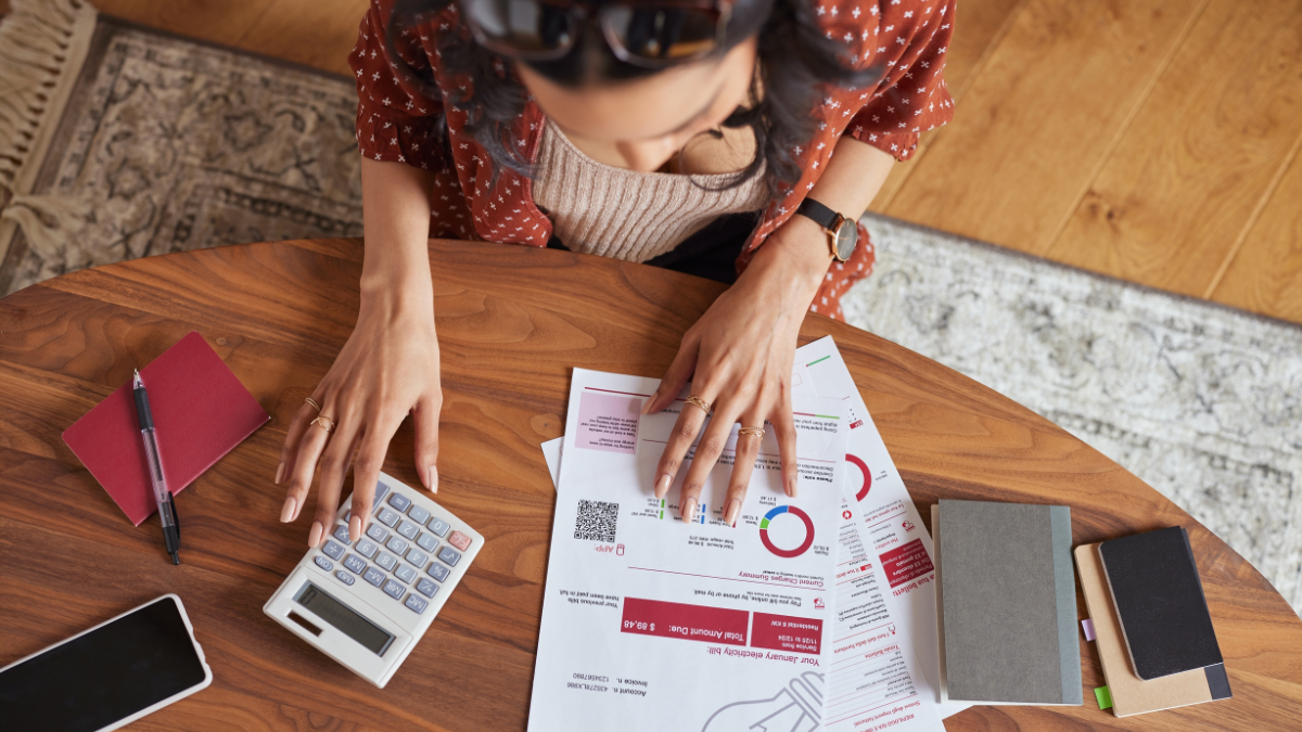 Top angle view of young woman calculating monthly expenses and checking electricity bill invoice while calculating using calculator. Latin girl examining the consumption and increase of electricity.