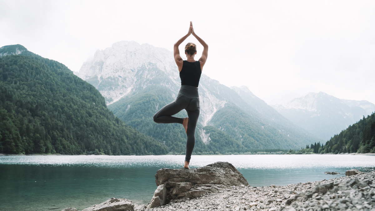 Young woman is practicing yoga at mountain lake. Girl doing yoga on nature. Healthy lifestyles. Concept of vitality, balance, mindfulness, zen energy, calmness, relaxation.