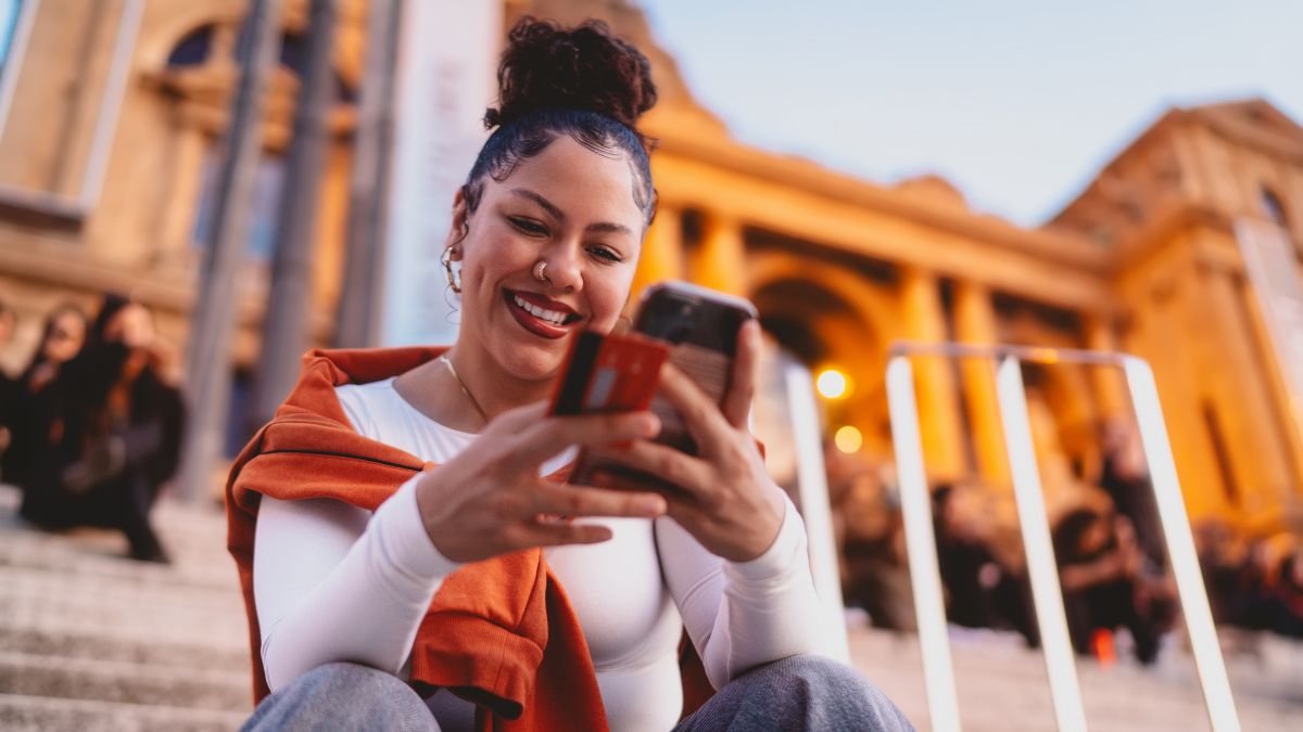 smiling woman enters payment details on her smartphone, making online purchase or paying bills. Female might also be managing finances, transferring money, or using a banking app for transactions.