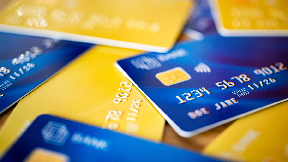 Stack of blue and yellow credit cards and shopping gift cards. Bank cards piled on table. Close up shot of group of debit and credit card: banking, digital payment and consumerism concept.
