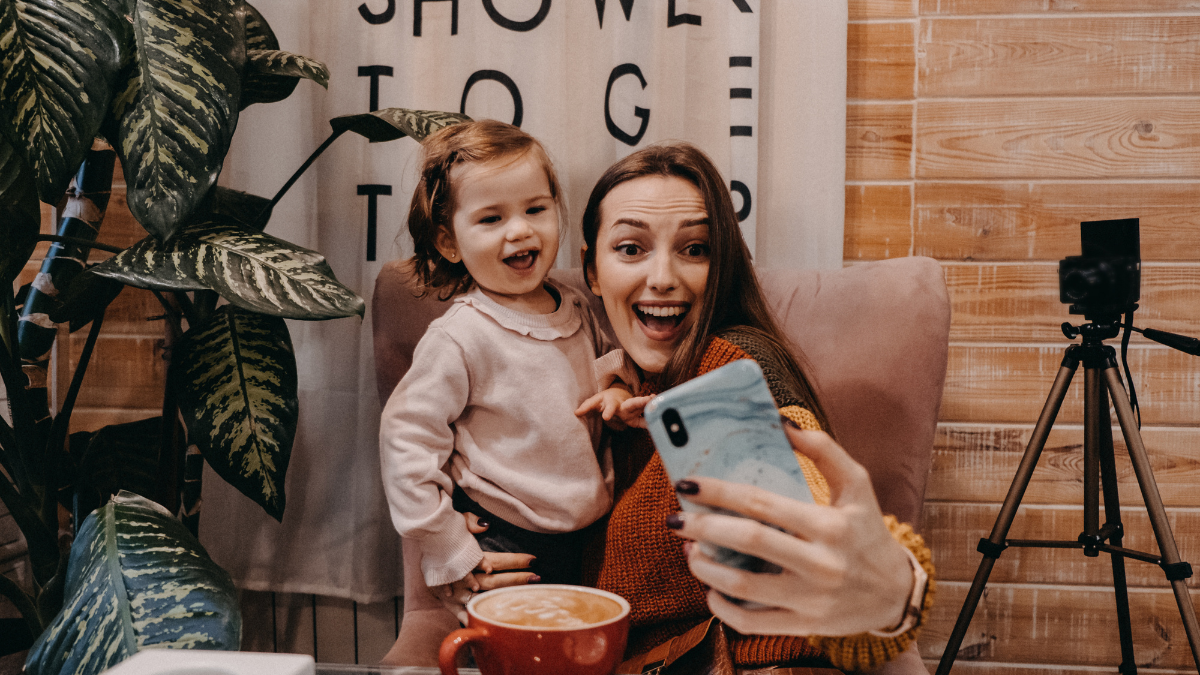 Online jobs for stay-at-home moms. Work From Home women with kids. Blogger girl and her little daughter have fun together. Young parenting blogger recording a video with her baby at home.