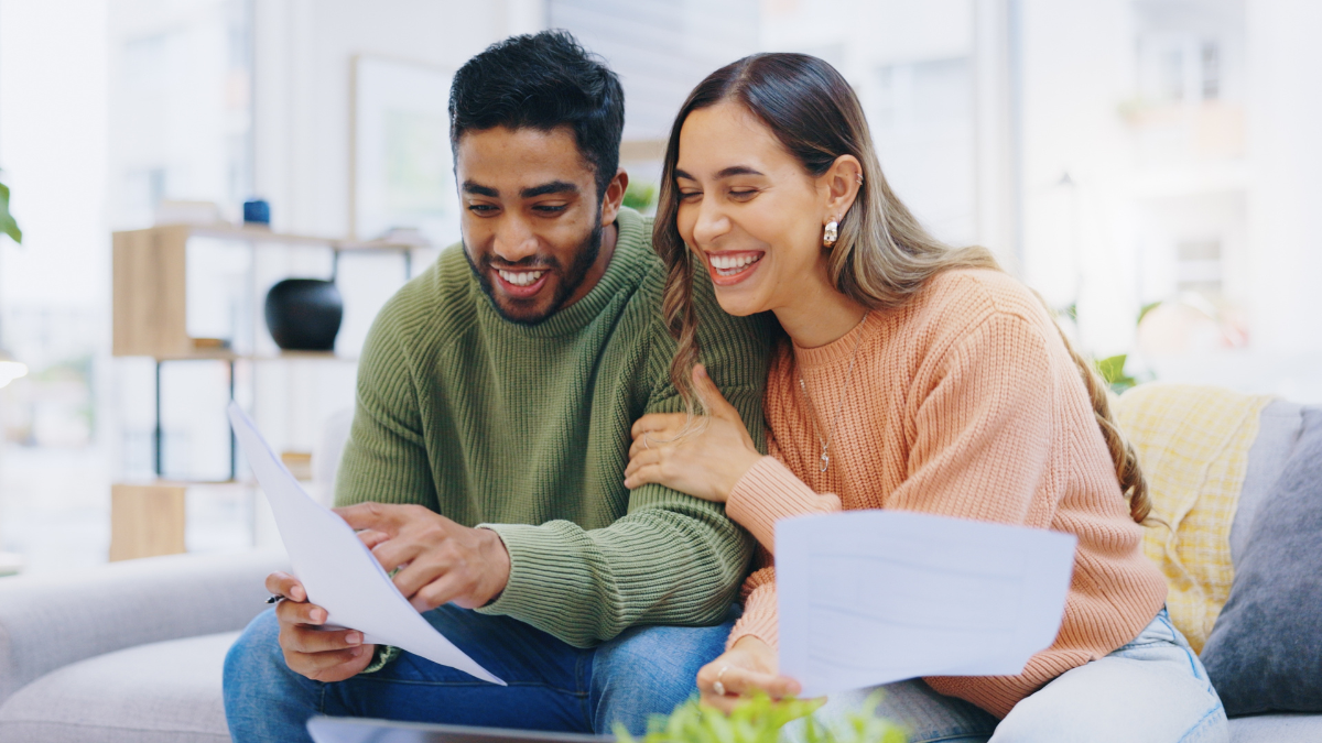 Couple, tax documents and happy on sofa with reading, review and compliance for financial freedom in home. Man, woman and smile together for results, feedback and free credit score with paperwork on couch.