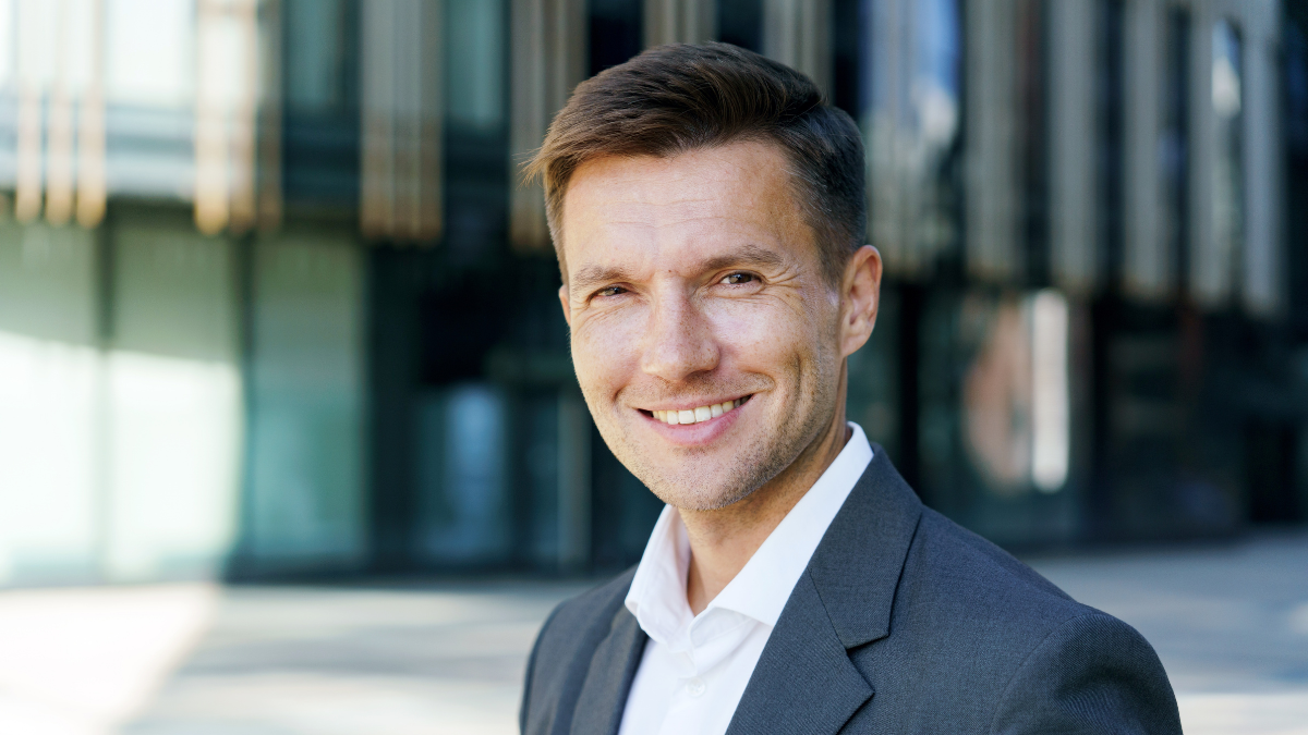 Confident businessman in a suit smiles at the camera outside a modern office building how to get rich.