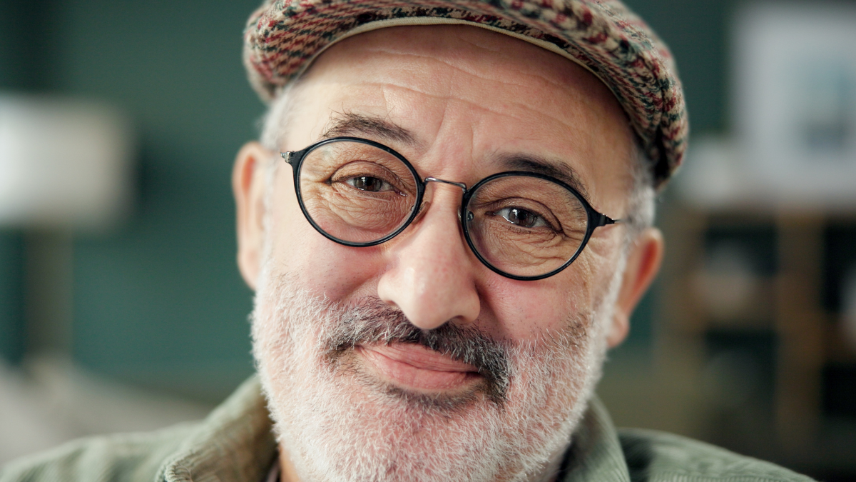 unearned income Portrait, smile and glasses with man in home for author, about us and confidence. Literature expert, pride and happiness with mature male person in living room of apartment for creative writer.