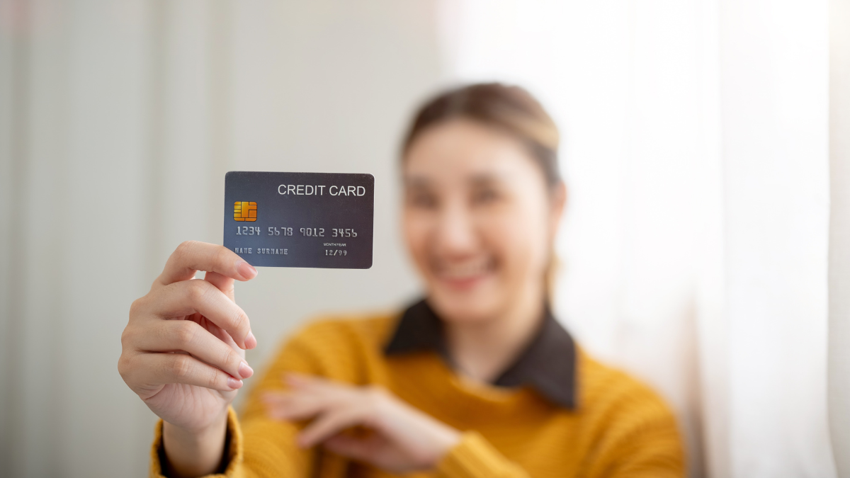 Blurred face young asian woman extending one hand holding and showing a credit card to camera. Travel card, Cashless society, Bank Advertising.