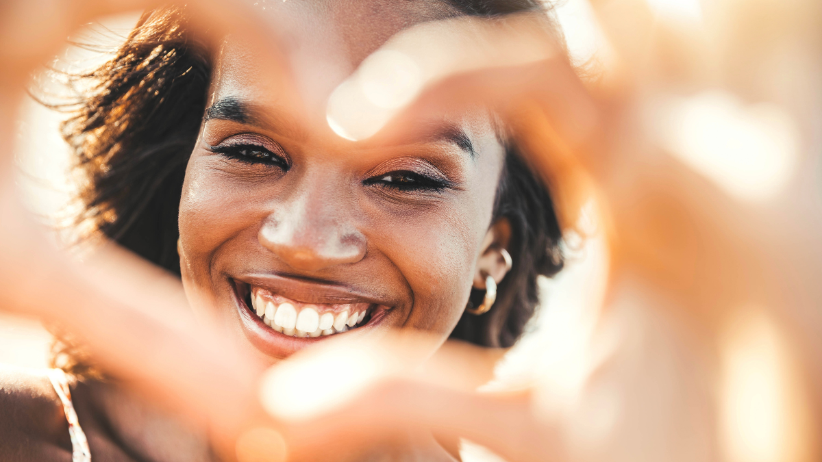 Beautiful young woman making heart shape with hands - Happy black woman smiling at camera outdoors - Health care and self love concept self care quotes.