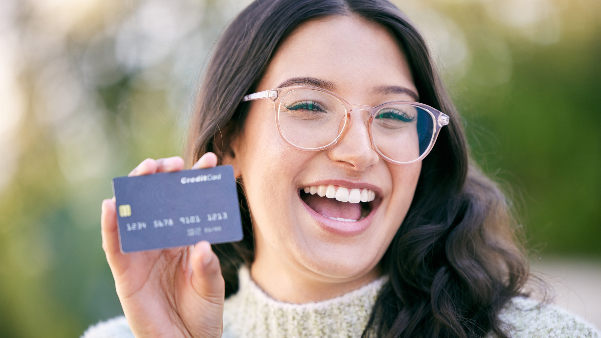 Happiness is banking with a bank who has your back. a happy young woman holding up a credit card while standing outside.