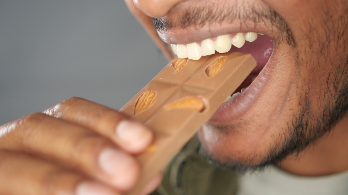 Man bites chocolate bar with nuts.