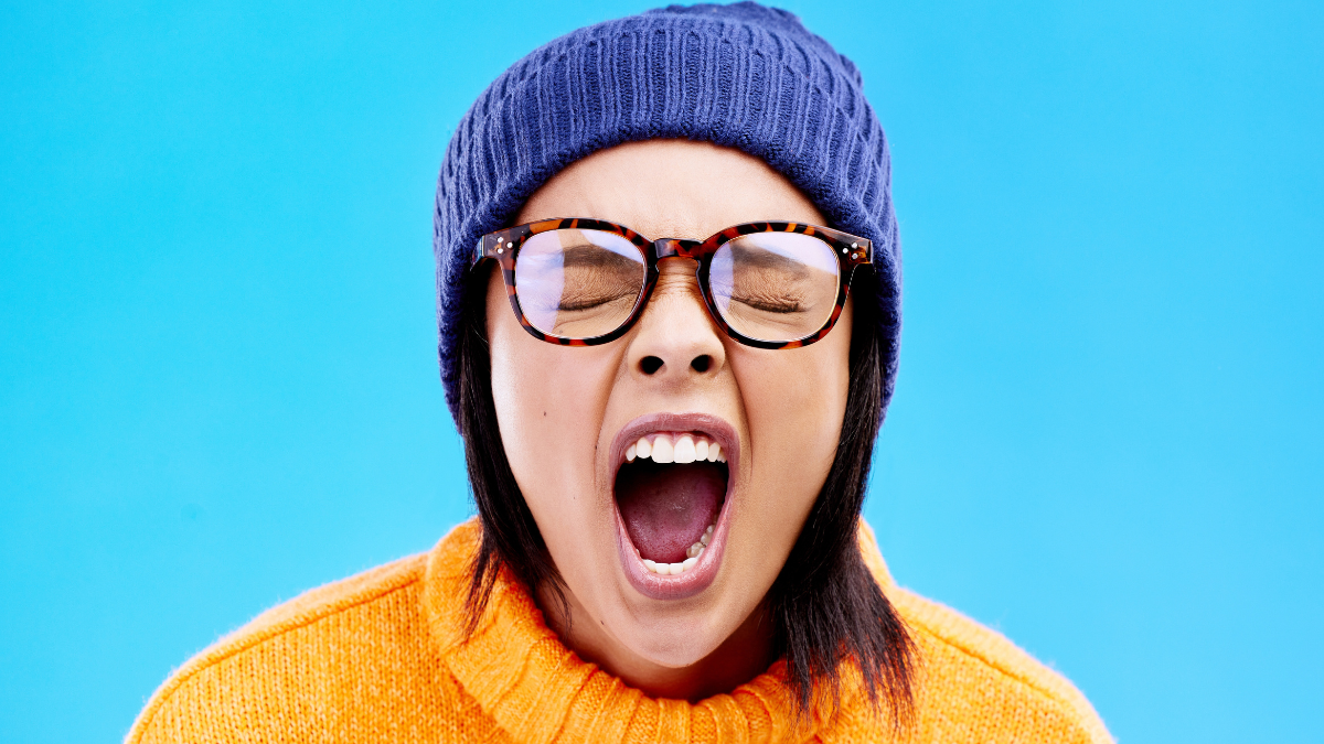 Portrait of woman in winter fashion, screaming with beanie and glasses isolated on blue background. Anger, frustration and face of frustrated gen z girl in studio with warm clothes for cold weather.