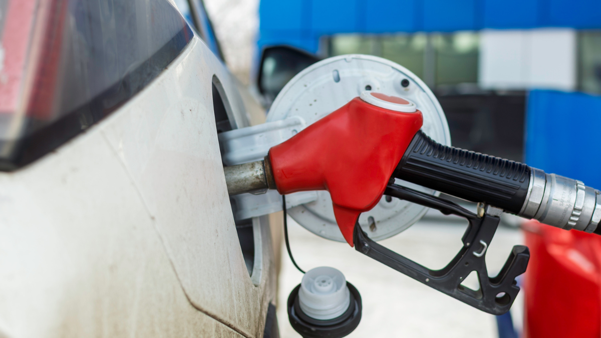 Red fuel nozzle inserted into dirty white car tank at gas station in winter, close-up view highlighting refueling process and everyday vehicle use saving money with gas apps.
