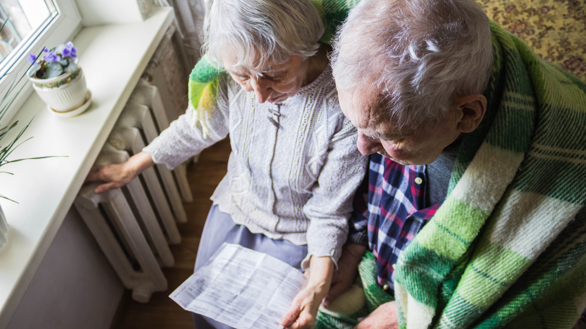 The senior woman holding gas bill in front of heating radiator. Payment for heating in winter..