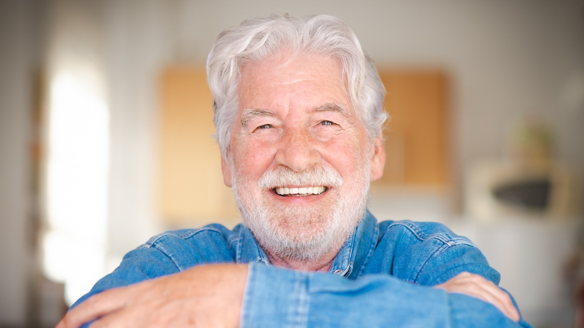 Portrait of beautiful senior bearded man smiling sitting at home with crossed arms looking at camera 401(K).