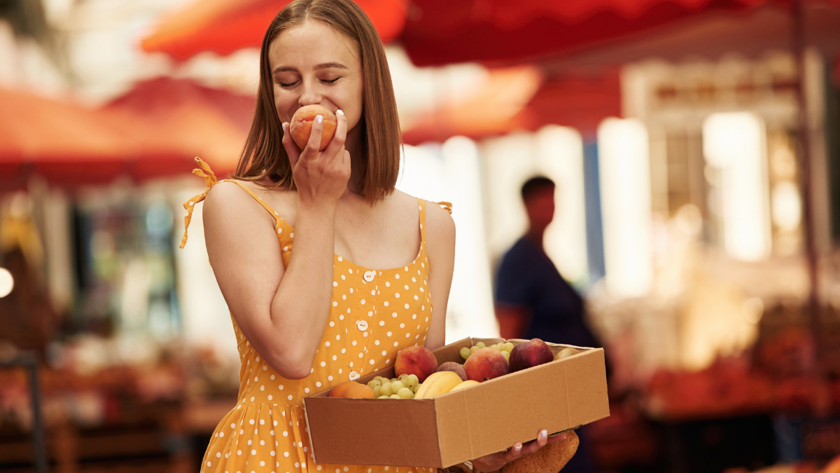 Box with peaches and grapes. Young woman is on the vegetable market or bazaar with free stuff.