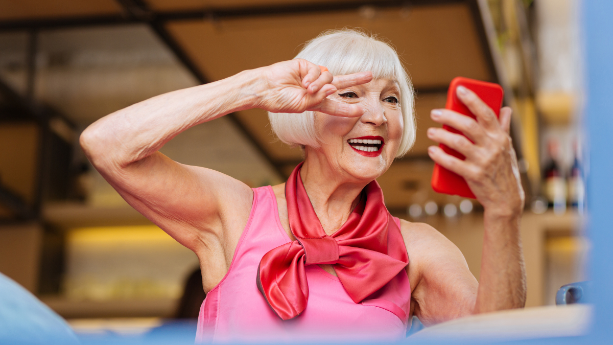 Fun selfie. Joyful senior woman looking into the smartphone camera while taking a selfie.