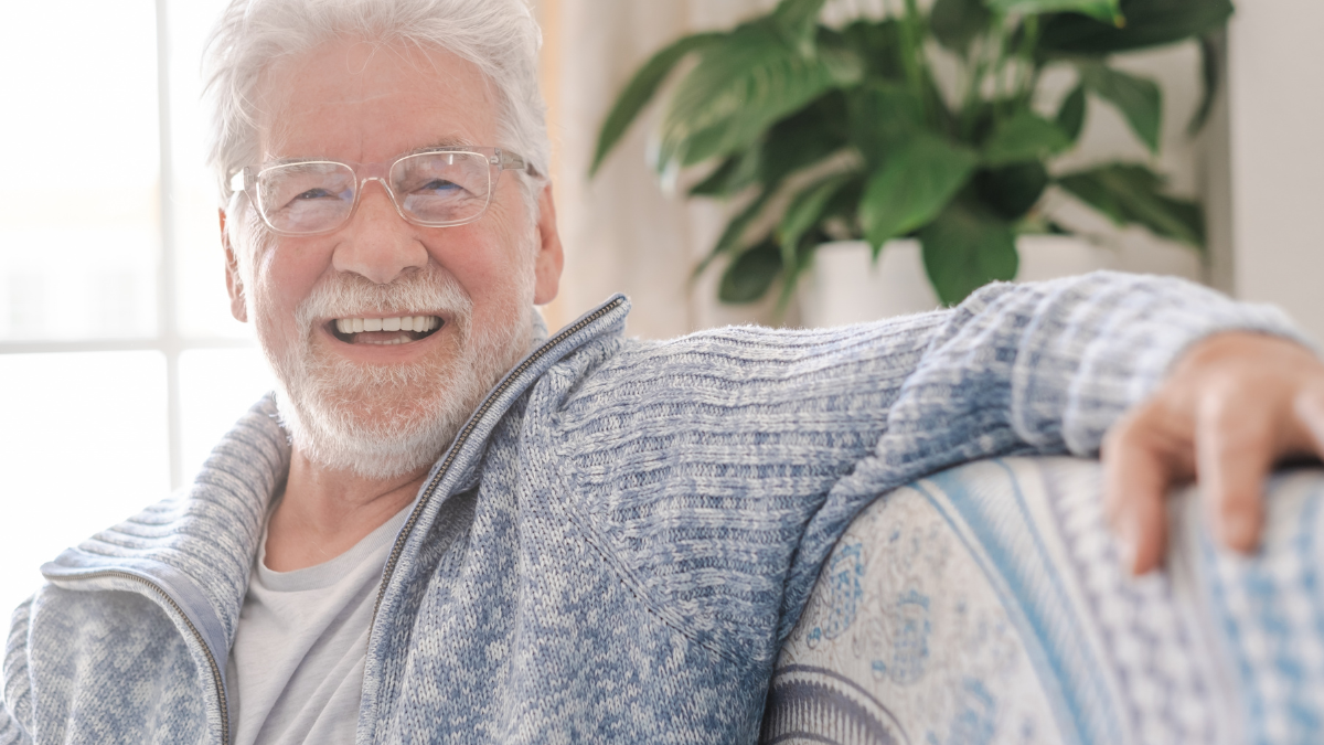 Portrait of happy senior man wearing eyeglasses smiling looking at camera. Old man relaxing on sofa at home. Portrait of elderly man enjoying retirement retirement checklist.