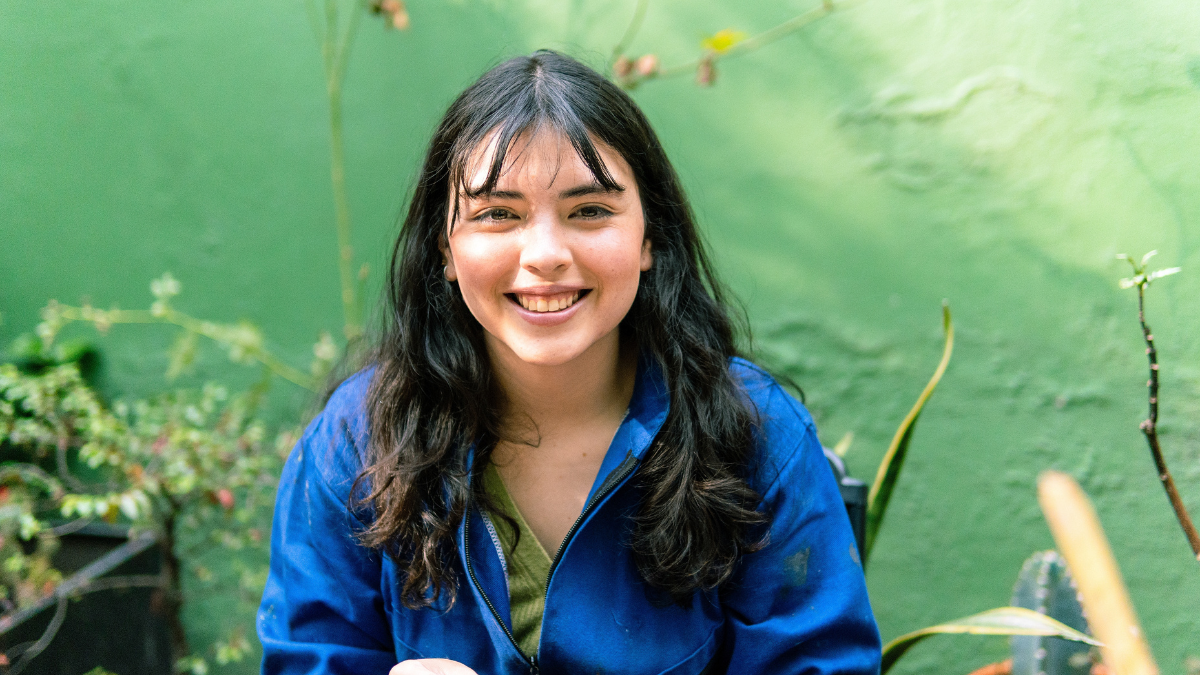 Smiling young woman gardener working diligently in a vibrant greenhouse, nurturing and caring for a variety of flourishing plants.
