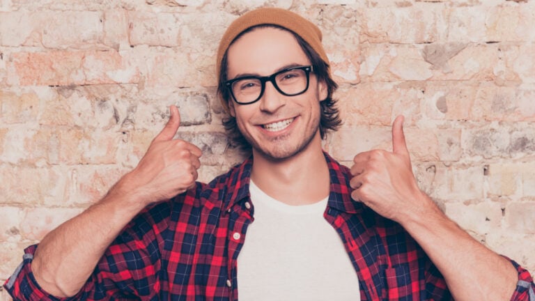 Portrait of happy hipster man showing thumbs up near brick wall.