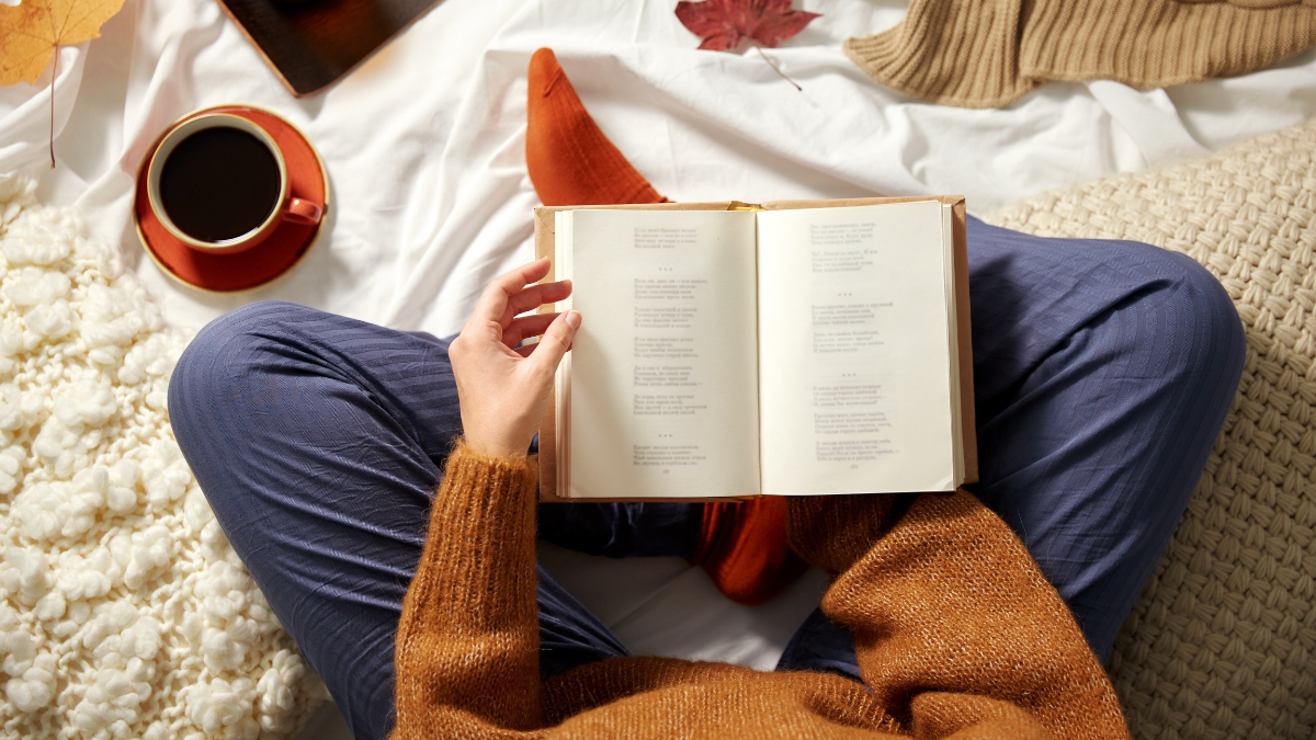 people, season and leisure concept - young woman reading book at home in autumn making reading a habit.
