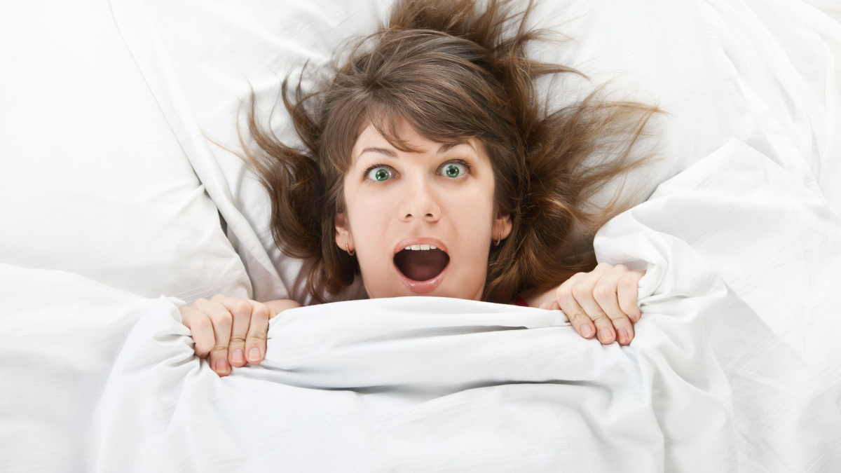 beautiful girl in bed at home hiding under a blanket with a surprised face.