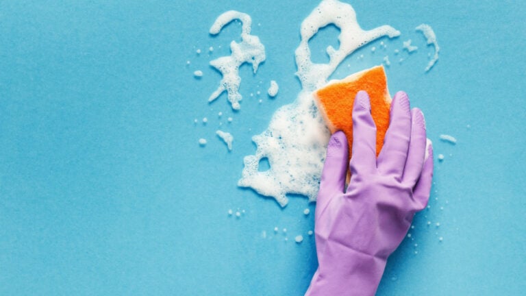 Cleaning concept - hand in orange protective rubber glove washing glass window with sponge and detergent foam. Householding background, copy space.