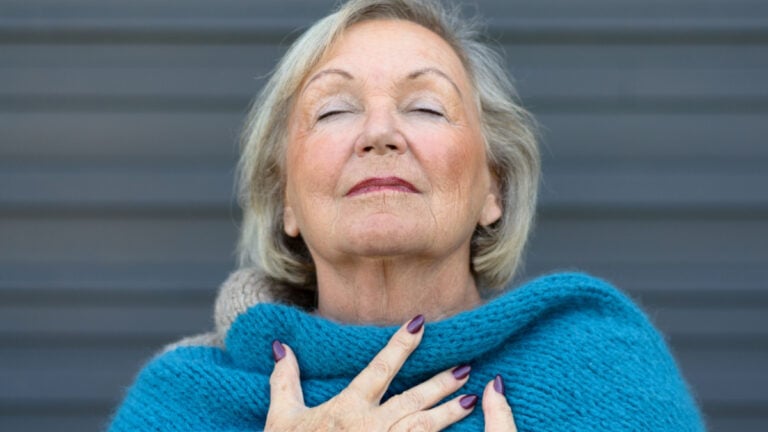 Attractive senior woman savoring the moment standing with her eyes closed and head tilted back with a serene expression as she clasps her chest with her hands.