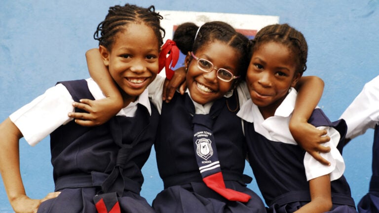 CIRCA 2010 Jamaica, Kingston, portrait of three African schoolgirls smiling with arm around.