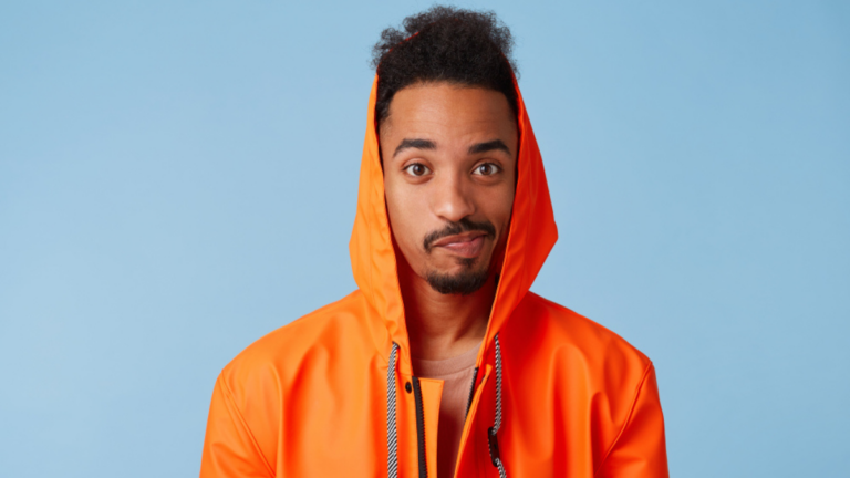 Unhappy handsome african american dark skinned boy wears in orange rain coat, confused, distressed by bad weather and spoiled weekend plans.