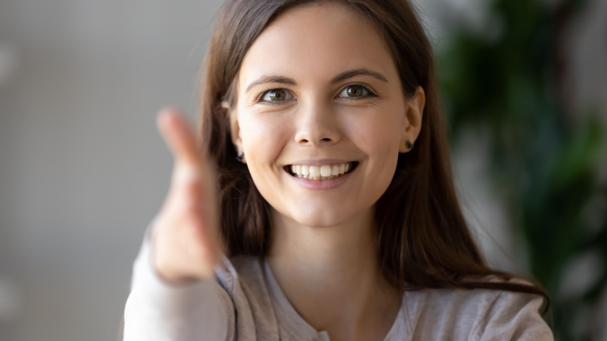 Smiling businesswoman holds out her hand to camera for handshake arm close up, focus on friendly face.