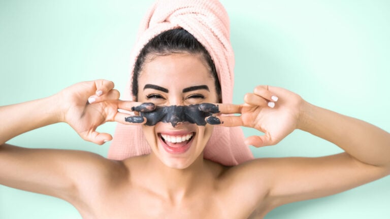 Happy smiling girl applying facial charcoal mask portrait.