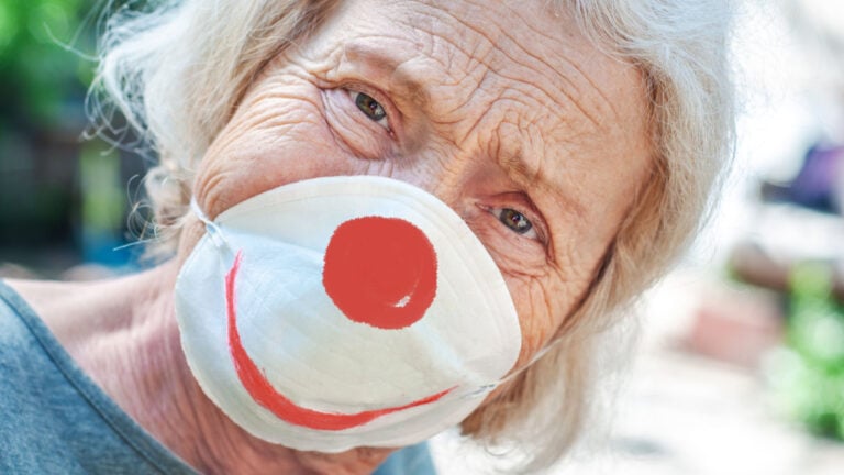 Angry sad grandmother elderly woman in a respiratory mask with a painted funny clown mask.