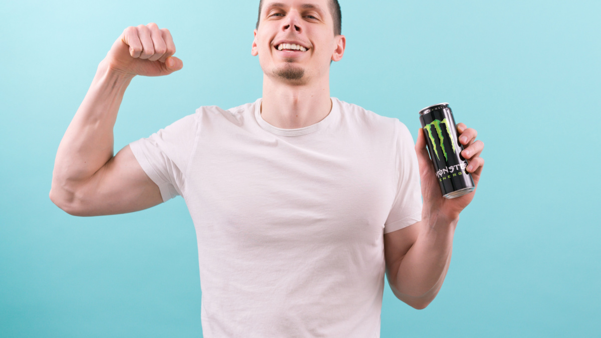 20 Things From the 90's That Haven’t Made a Comeback Yet 6 Corona, USA - Jun 9, 2022: A man in a white t-shirt smiles, holds a Monster black aluminum can, and shows a biceps on a blue background.