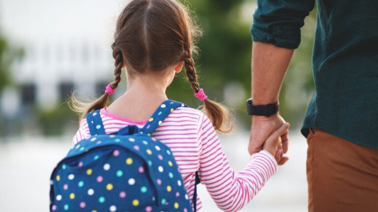 first day at school. father leads a little child school girl in first grade.