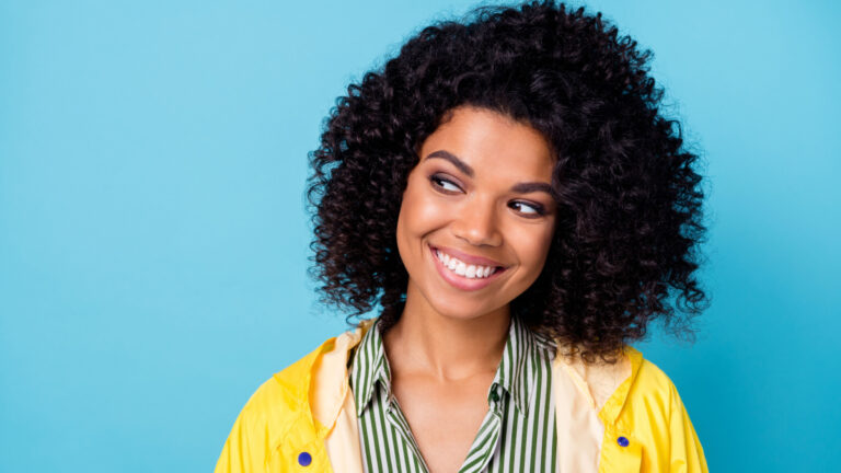 Photo of young cheerful black woman happy positive smile wear raincoat look empty space isolated over blue color background.