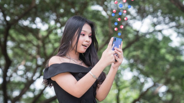 A young woman is elated to get many positive reactions on her social media post. Standing outside at a park.
