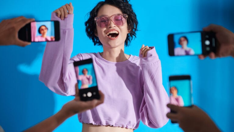 Teenage girl singing with people photographing her in smartphones.