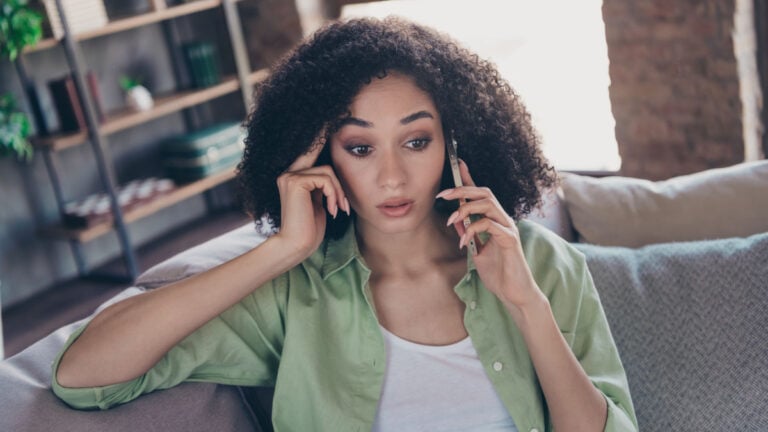 Portrait of confused impressed girl sitting sofa speak communicate telephone unbelievable information loft interior apartment inside.