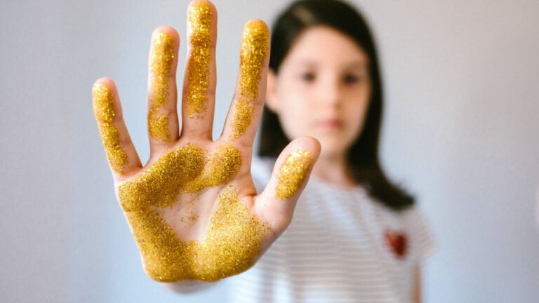 Serious young girl showing her palm hand covered of golden glitter while doing stop sign.