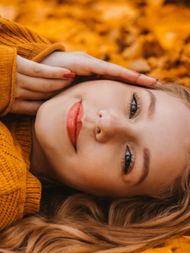 Beautiful girl lies in autumn leaves in the park, autumn. Young girl with perfect skin in a yellow sweater looks at the camera.