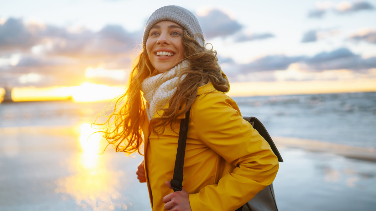Happy tourist in a yellow jacket posing by the sea at sunset. Travelling, lifestyle, adventure.