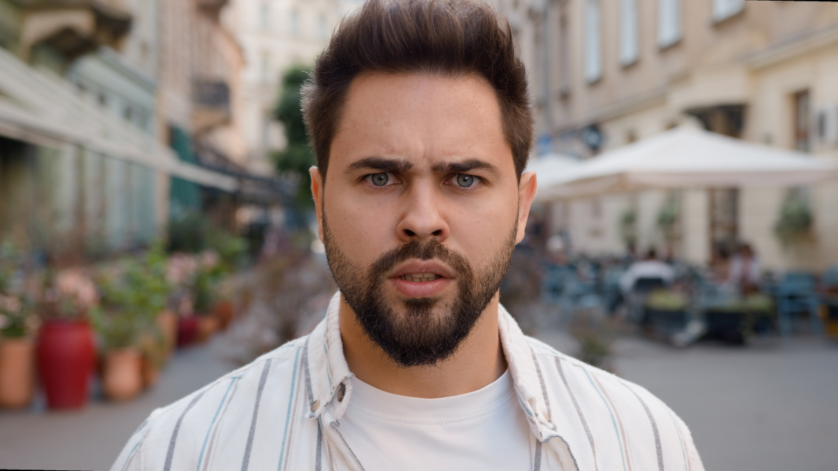 Close up angry Caucasian man frowning eyebrows city street outside dissatisfied displeased disappointed male problem trouble conflict emotion serious anger feeling frustrated guy hard negative annoyed,