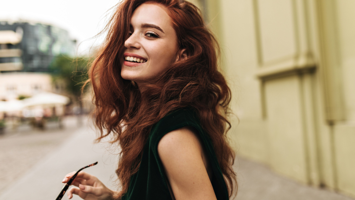 Attractive woman in dark green outfit smiling outside.