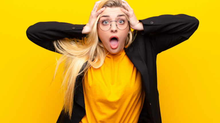 young pretty blonde woman feeling horrified and shocked, raising hands to head and panicking at a mistake against yellow wall.