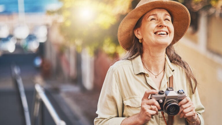 Happy photographer tourist taking photo of historic building with camera, smiling and carefree. Excited mature female solo travel journey, enjoying retirement while looking at bucket list.