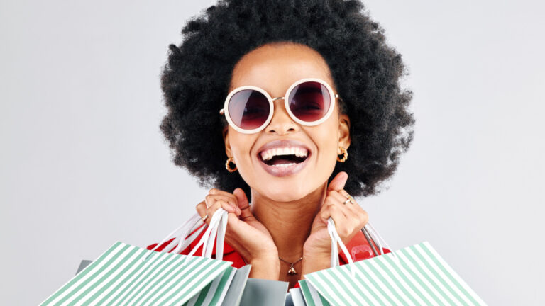 Happy black woman, face and shopping bags for fashion or style against a white studio background.