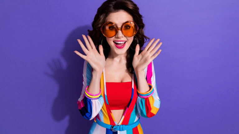Photo of funky shocked girl dressed striped overall dark eyewear rising hands arms isolated violet color background.