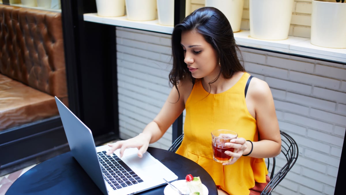 Portrait of a young female freelancer using laptop computer for distance job while sitting in modern coffee shop interior, smart brunette woman working on net-book during morning breakfast in cafe bar.