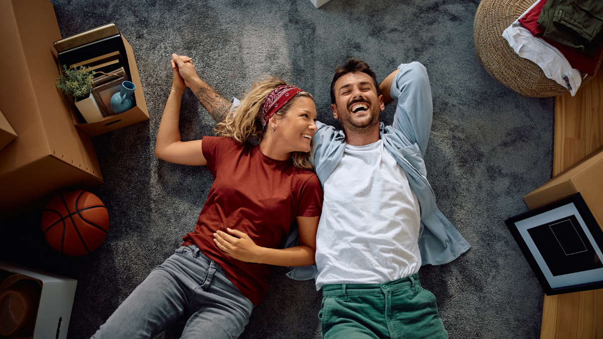 high angle view of cheerful couple lying down on the floor in their new home. fun while being frugal.