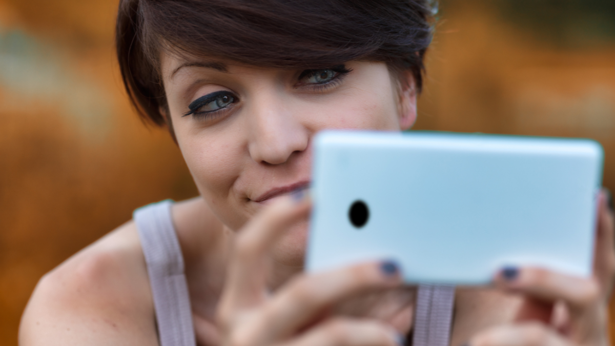 Sceptical young woman looking at her mobile phone with a wry smile and expression of disbelief in a close up cropped portrait.