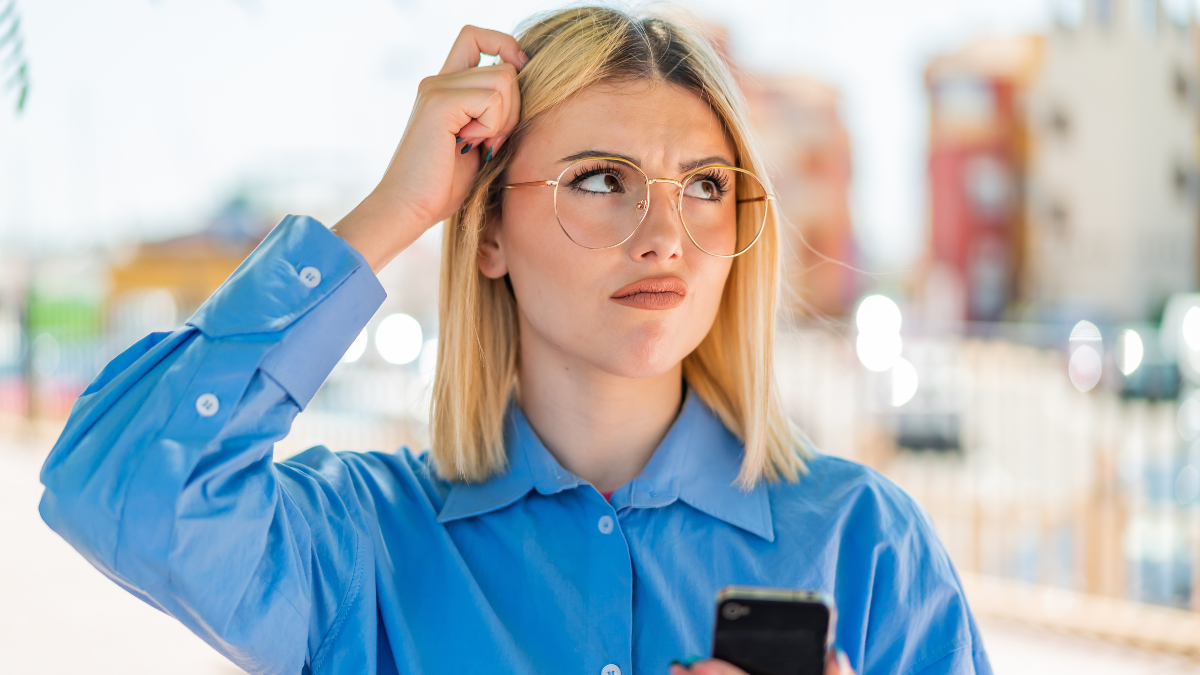 Young pretty blonde woman using mobile phone at outdoors having doubts and with confuse face expression.