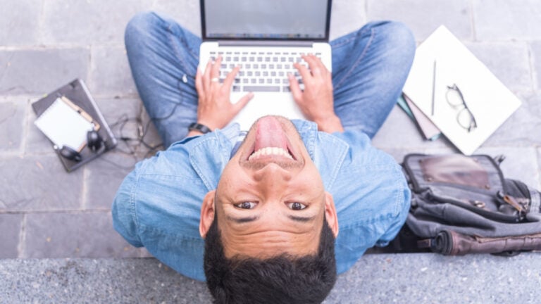 Funny and crazy freelancer man using a laptop computer typing keyboard and making funny faces, top view and blur background.